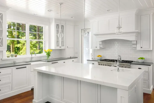 White kitchen with island, cabinets, and appliances. Large window with natural light.