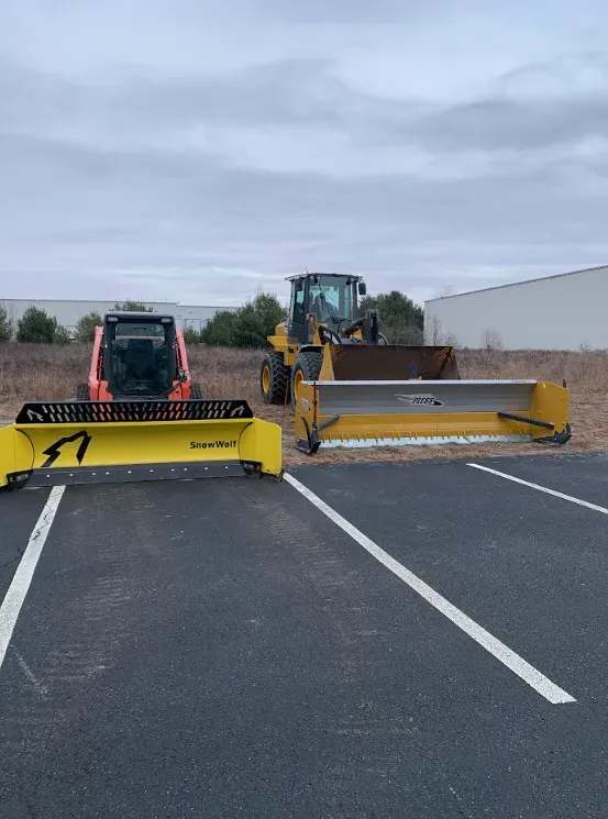 Two snow plows and a skid steer parked on a parking lot under an overcast sky