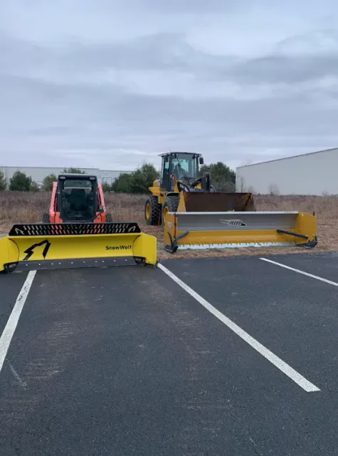 Two snow plows and a skid steer parked on a parking lot under an overcast sky