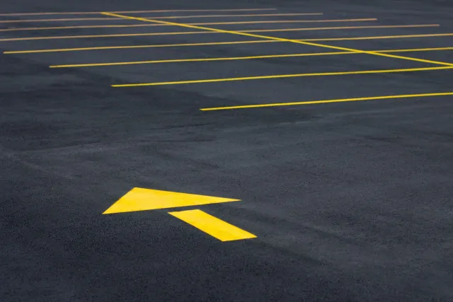 A parking lot with painted yellow lines marking spaces and a large yellow arrow pointing forward on the asphalt.