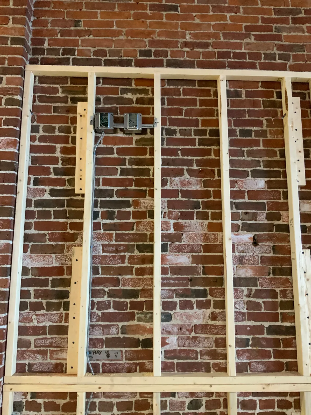 Brick wall with wooden framing and electrical boxes in progress of construction or renovation.