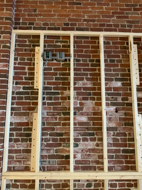 Brick wall with wooden framing and electrical boxes in progress of construction or renovation.