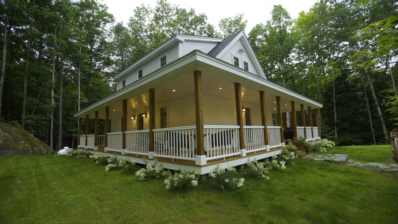 Custom home with a wraparound porch surrounded by lush greenery, built by Oxland Builders in New Hampshire