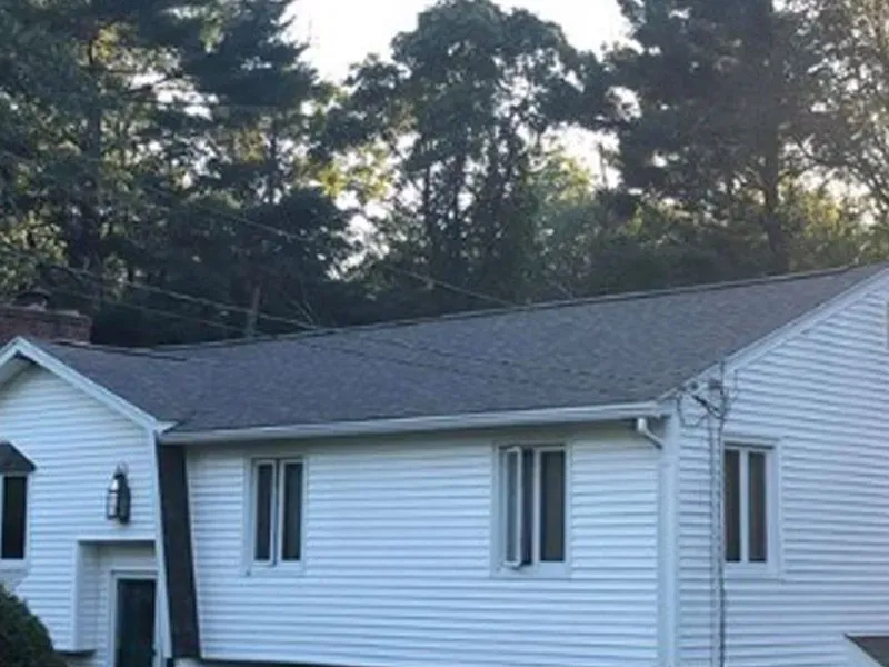 White single-story house with gray roof and trees in the background