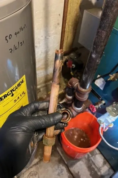 Gloved hand holding corroded copper pipe and fitting