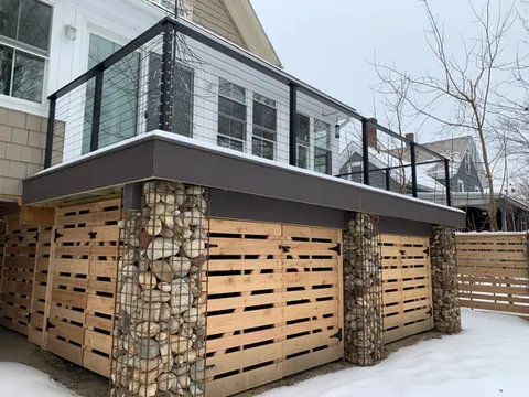 Custom cedar gabion fence and Trex deck with stone-filled columns by Peri's Line