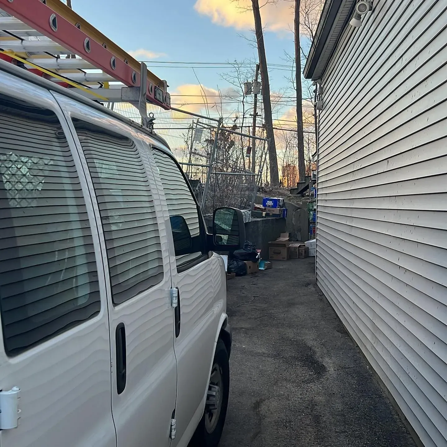 A white van with a ladder on top of it is parked next to a white house.