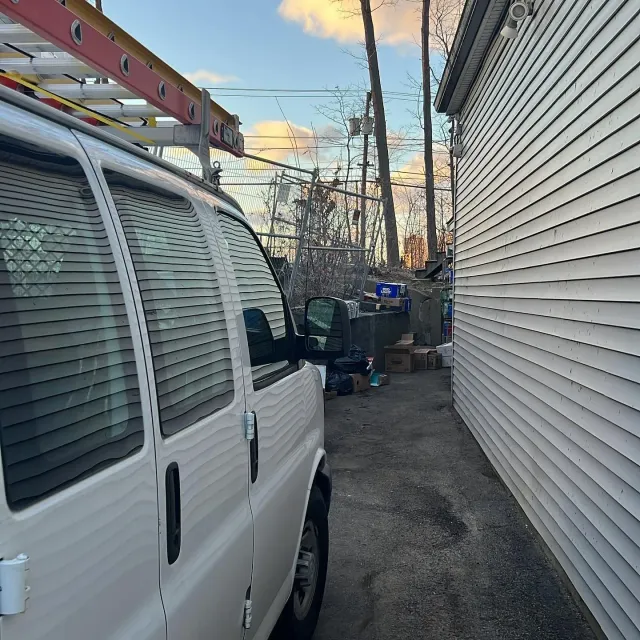 A white van with a ladder on top of it is parked next to a white house.