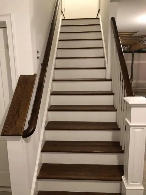 Narrow indoor staircase with white walls, dark treads, and wooden handrails