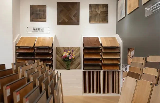 Art gallery with rows of wooden display racks, framed art on walls, and a flower arrangement in the center.