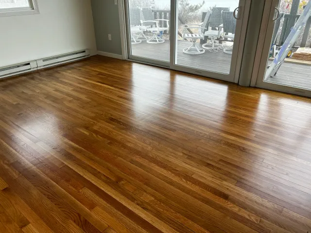 Room with polished hardwood floor, sliding glass doors leading to an outdoor deck with outdoor furniture, and a ladder outside.
