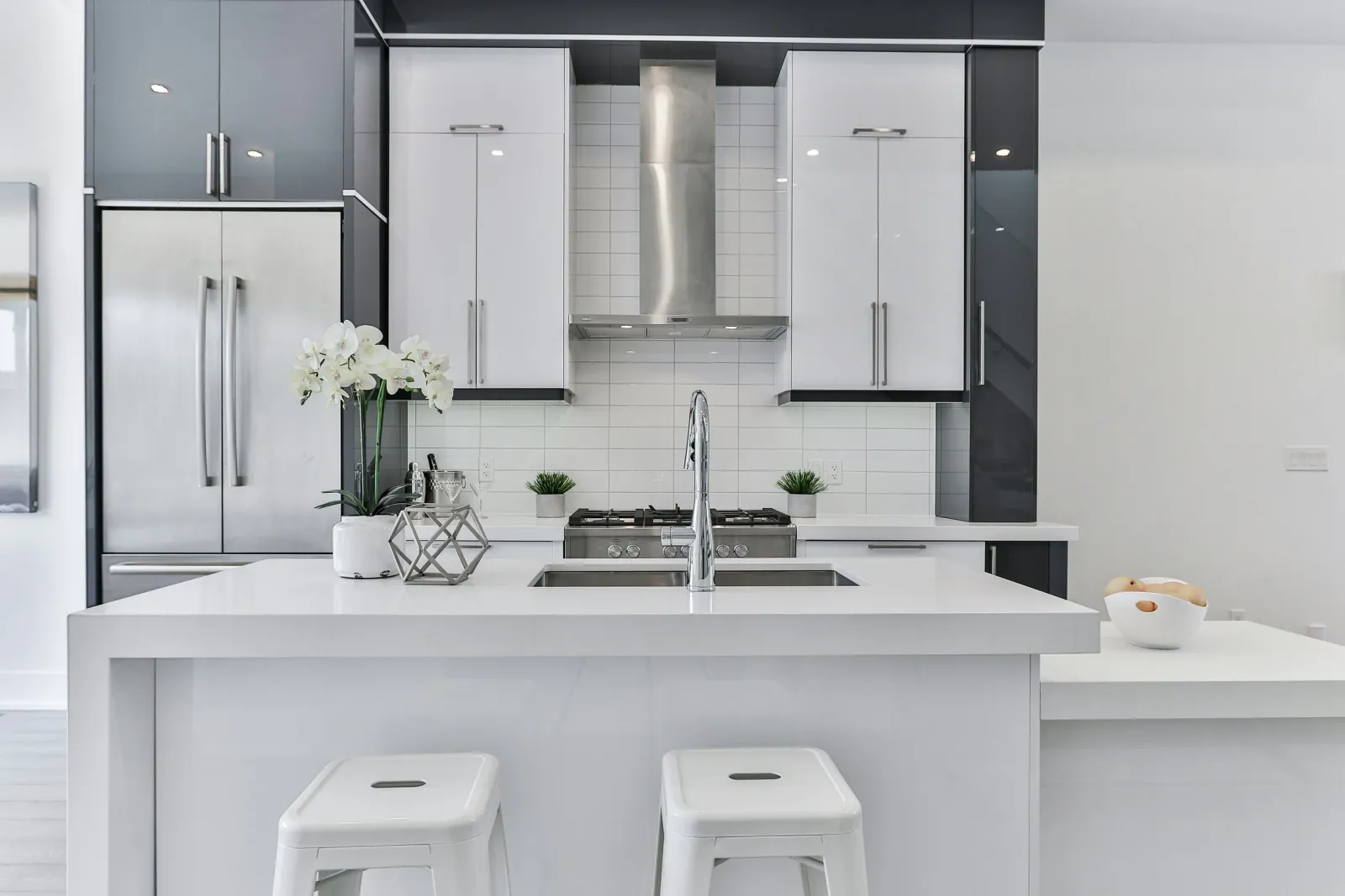 Modern kitchen with white island counter, stainless steel appliances, black and white cabinetry, and decorative plants.