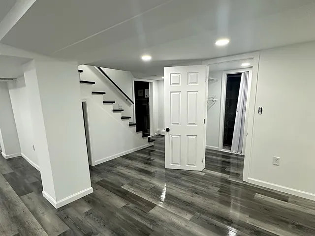 Finished basement in Prospect Connecticut with grey wide-plank vinyl flooring, bright white walls and trim, recessed LED lighting, an open painted stair run, and a new six-panel closet door