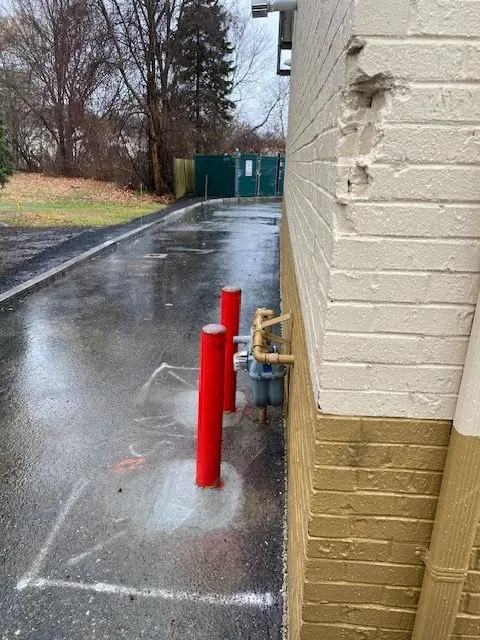 Rainy alley beside a building with red utility pipes and a green gate in the distance