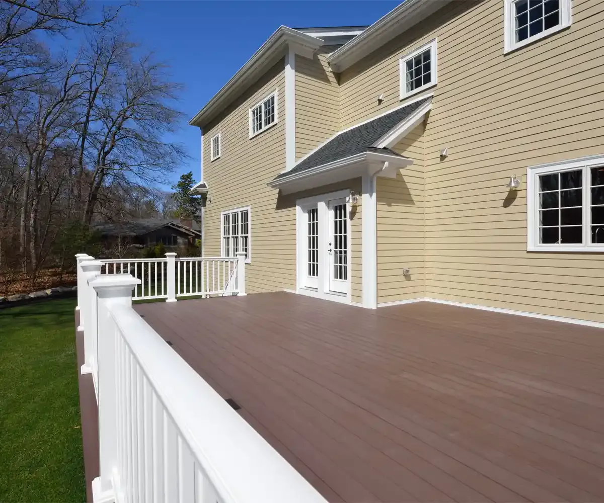Brown composite deck with white vinyl railing attached to a tan two-story home with French doors