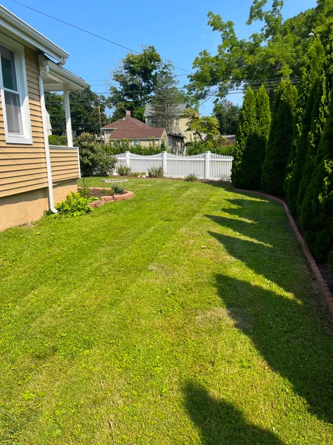 Side lawn with brick-edged beds and evergreen privacy hedge