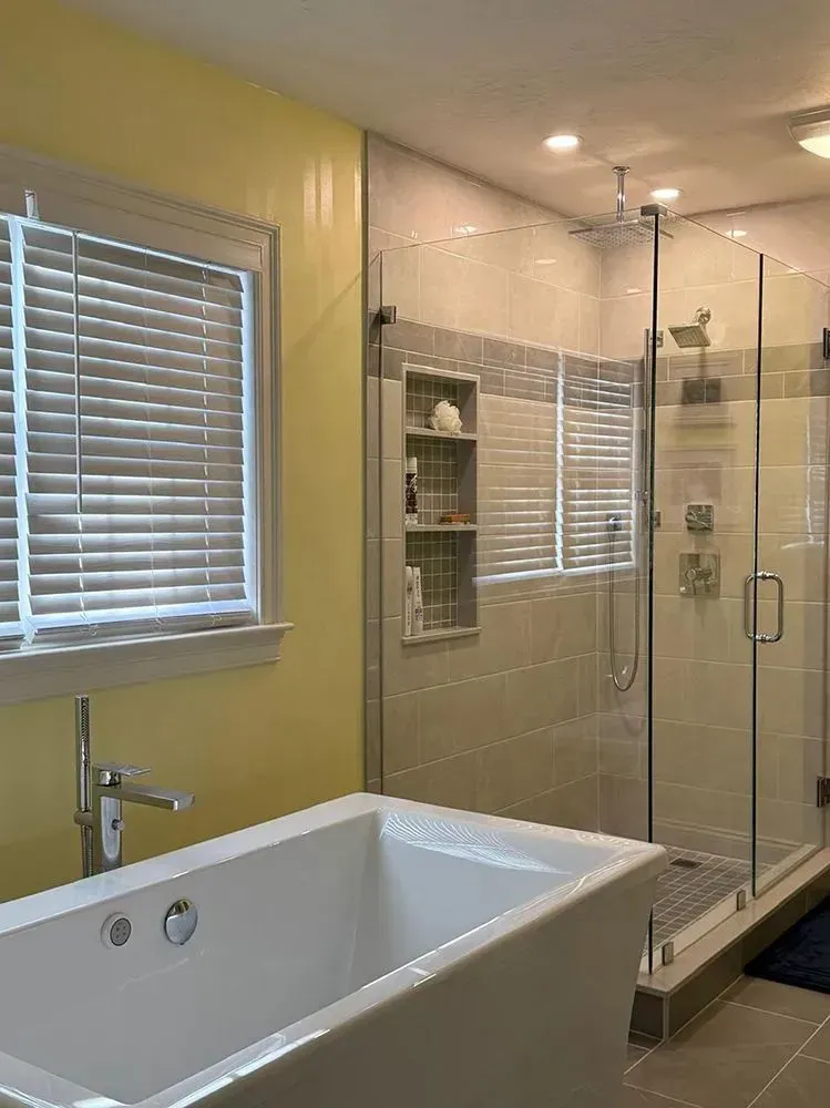 Bathroom with a white tub, glass shower, and yellow wall.