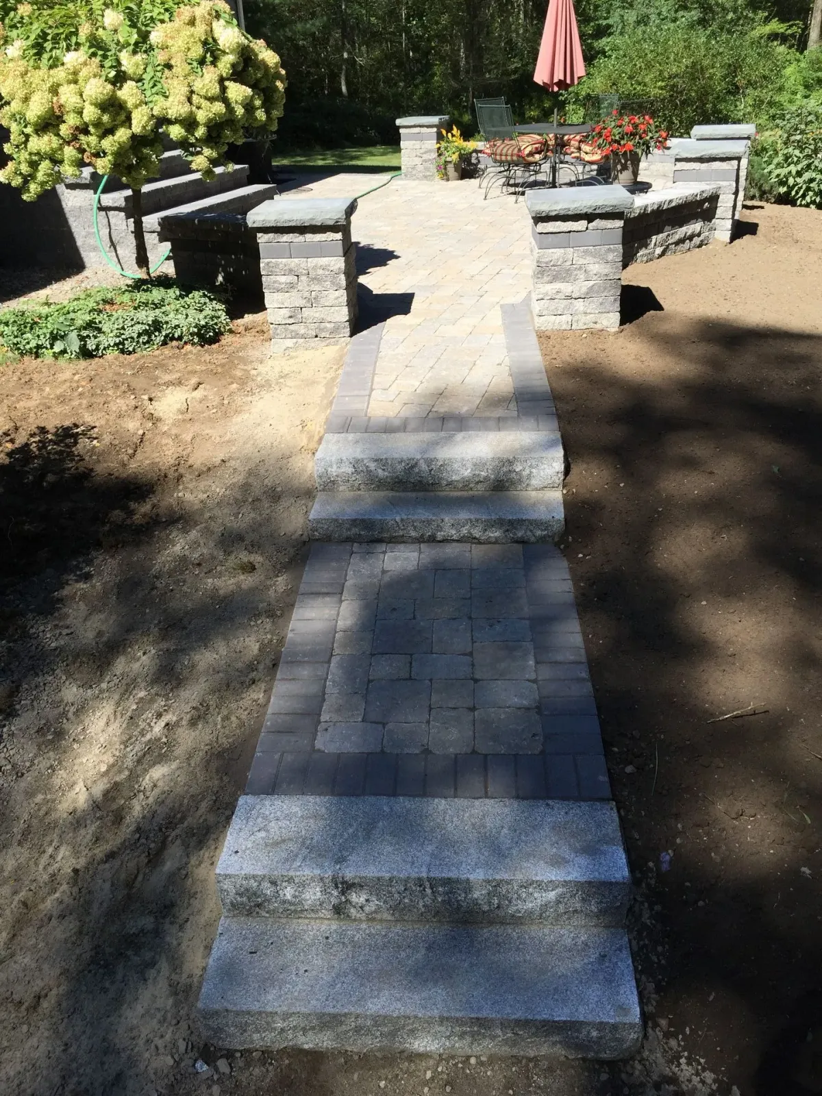 A brick walkway leading to a patio with a red umbrella in the background.