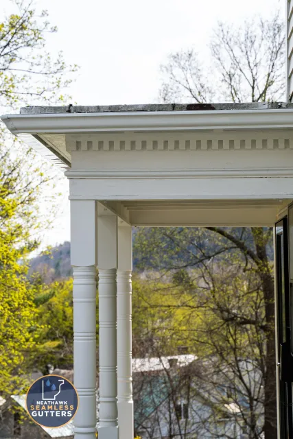 Close-up of a white porch with decorative columns and a seamless gutter system, featuring a logo for Neathawk Seamless Gutters.