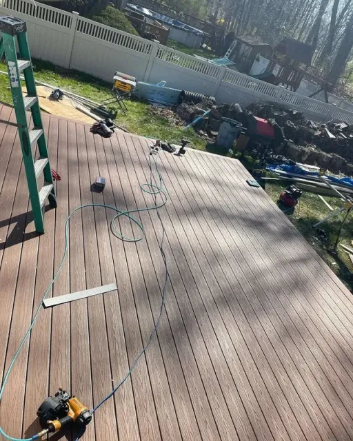 Brown wooden deck with tools, a ladder, and a green yard under construction.