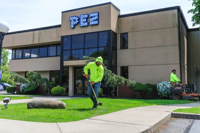 Two men working on the lawn in front of the PEZ factory; one rakes, the other mows.