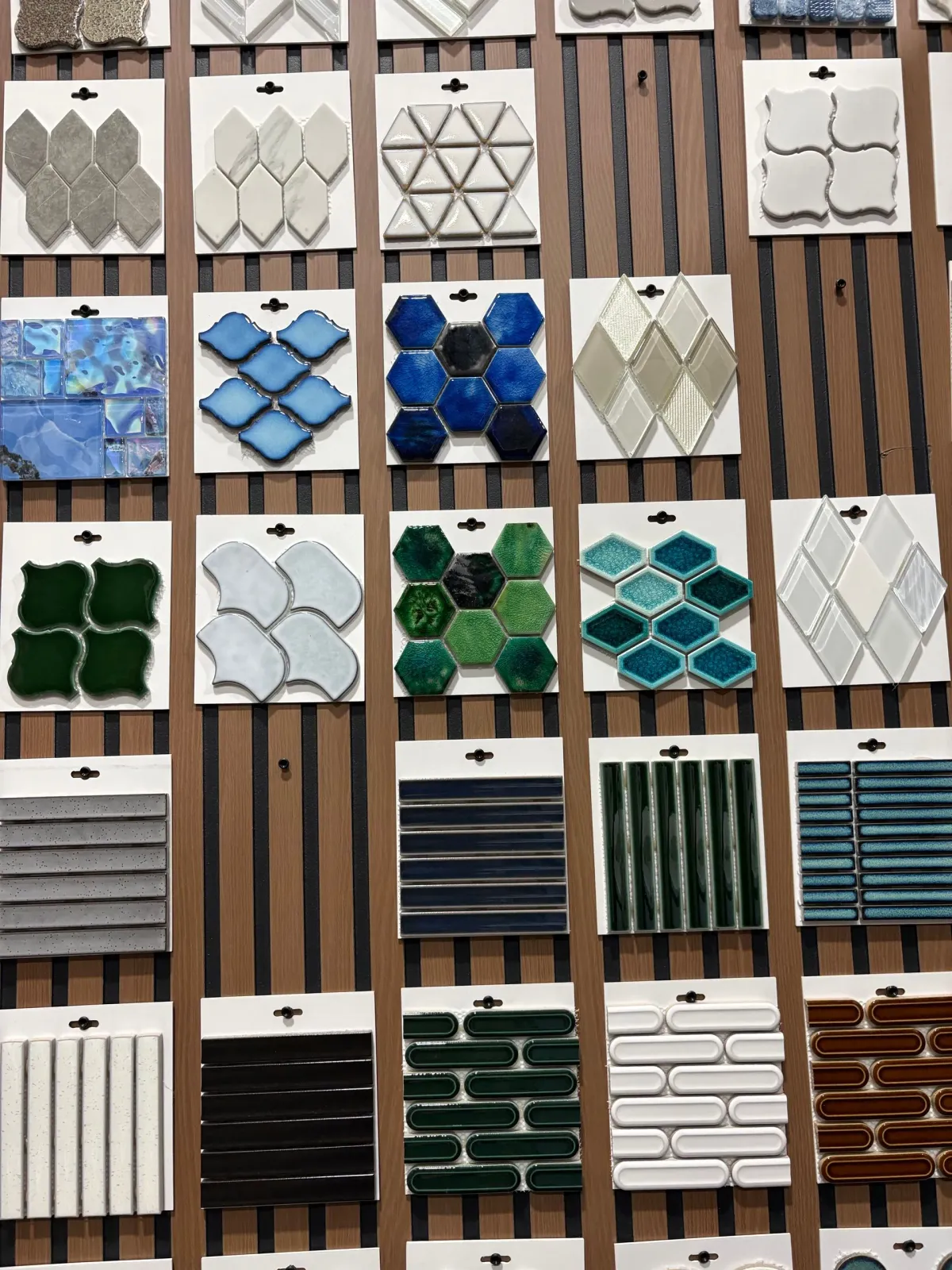 Grid of colorful geometric tile samples on a display board, featuring blue, green, white, and striped patterns.