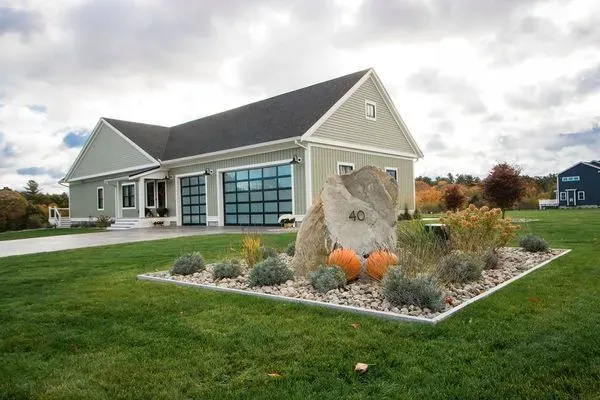 Light green house with glass garage doors, large rock, fall decor on lawn.