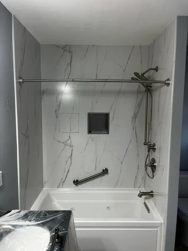 Finished tub surround in marble-look composite panel with shower column, niche and grab bar