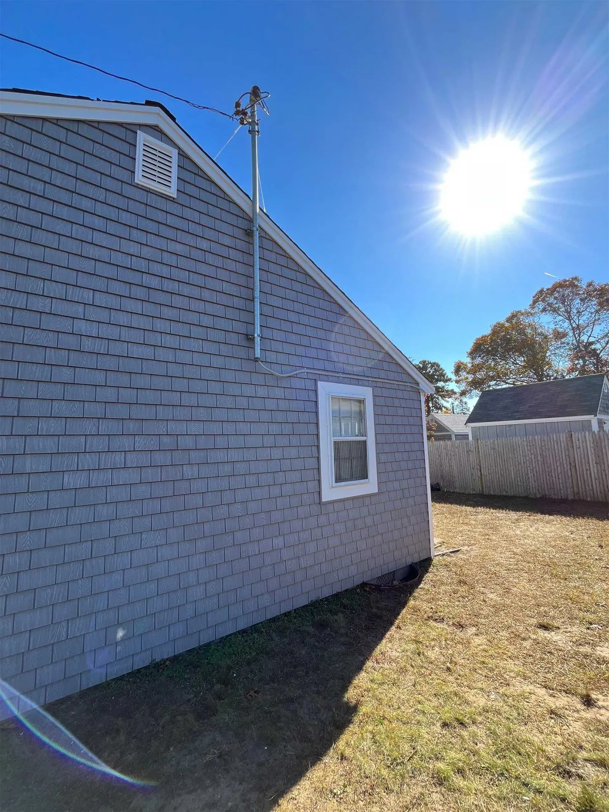 Side view of a home with gray shake siding, white trim, and utility mast