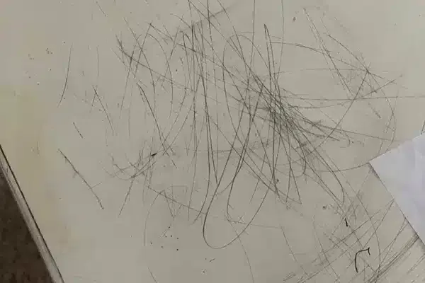 Messy pencil scribbles on a white surface next to a partially visible sheet of paper.