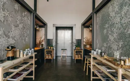 A narrow hallway with tables, trays, and jars lining both sides, leading to a closed door.
