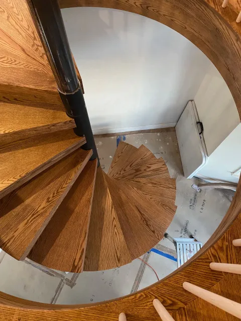 Looking down a spiral staircase with wood steps, black central pole, and white walls.
