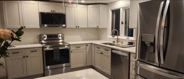 Modern kitchen with white cabinets, stainless steel appliances including a microwave, oven, and refrigerator, and a double sink near a window.