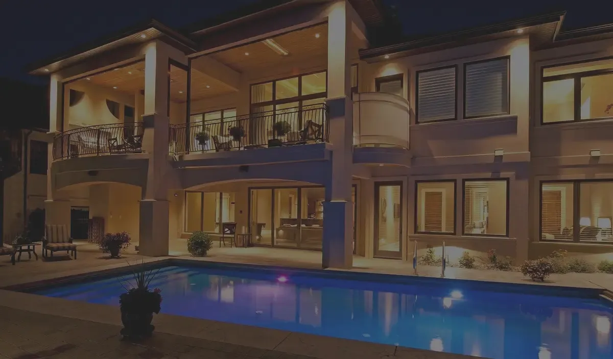 Large home glowing at night with landscape and interior lighting around a backyard pool