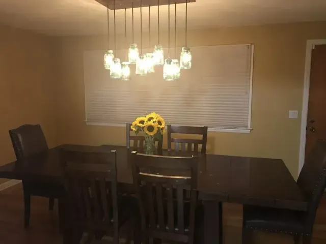 A dark wood dining table and chairs set under a multi-pendant mason jar light fixture, with sunflowers in the center.