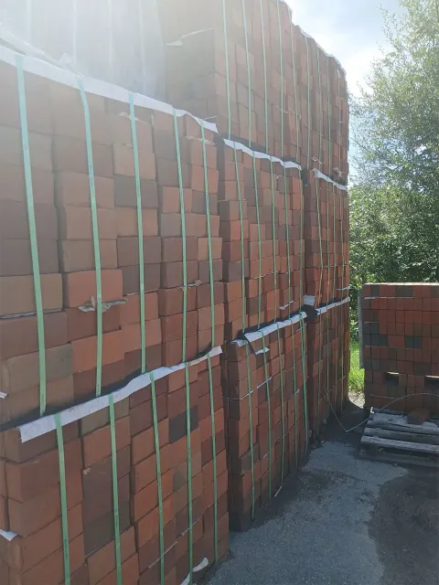 Stacks of red bricks secured with green straps, outdoors.