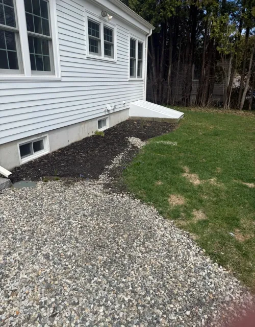 Backyard with a house, new gravel pathway, lush green grass, small garden bed, and wooded backyard.
