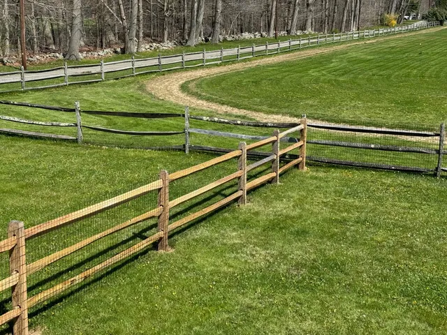 A wooden fence surrounds a grassy field with a dirt road going through it.