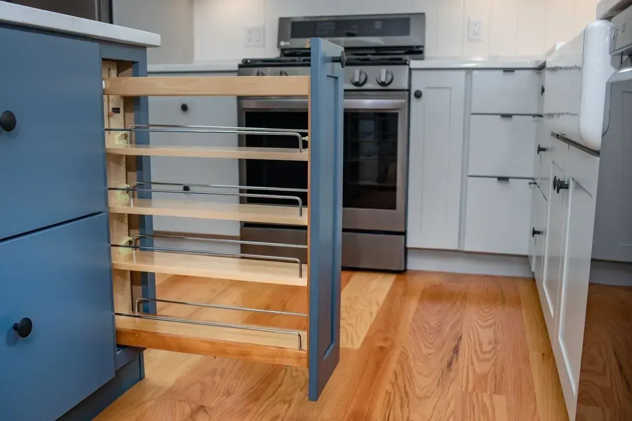 Kitchen with a pull-out pantry drawer and white cabinets beside a stainless steel oven.