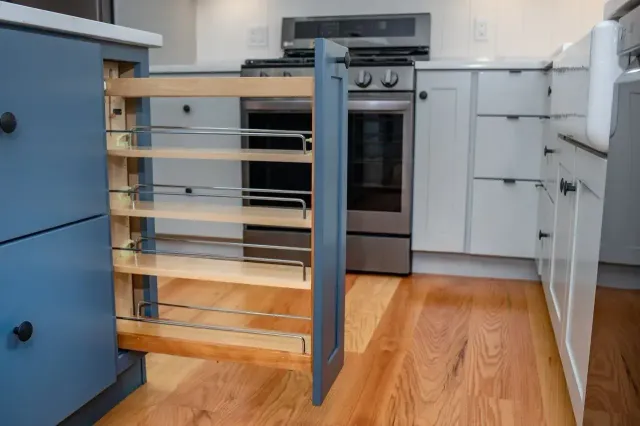 Kitchen with a pull-out pantry drawer and white cabinets beside a stainless steel oven.