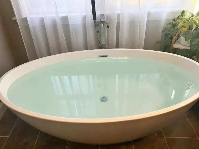 A bathtub filled with blue water in a bathroom next to a window.