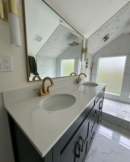 Modern bathroom vanity with gold faucet, dark cabinets, and slanted ceiling with skylight.