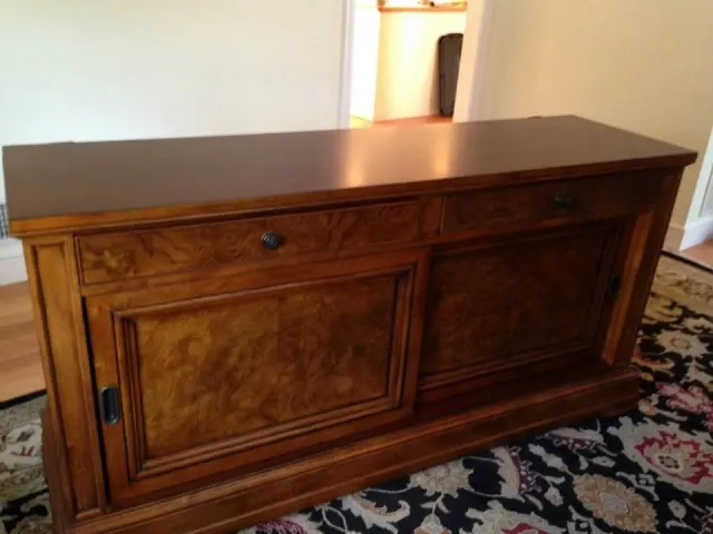 A dark wood sideboard with two drawers and two cabinet doors, sitting on a patterned rug in a home interior.