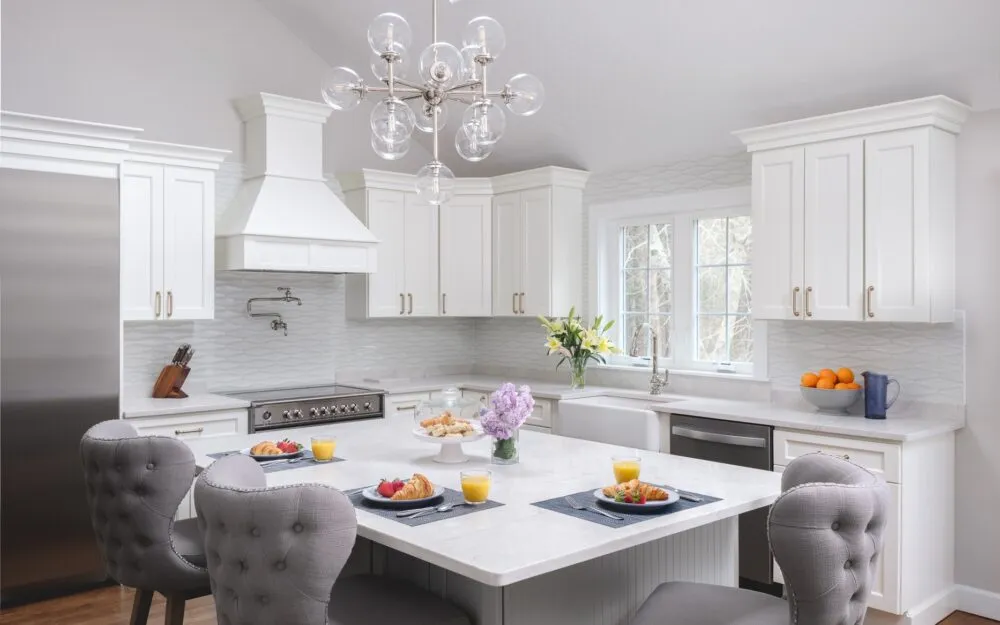 Bright, modern kitchen with white cabinets, stainless steel appliances, and a breakfast spread – Woodland Builders, South Shore MA.