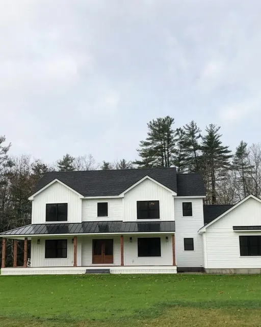 New two-story house with white exterior siding, black roof, and front porch, surrounded by a green lawn and trees.