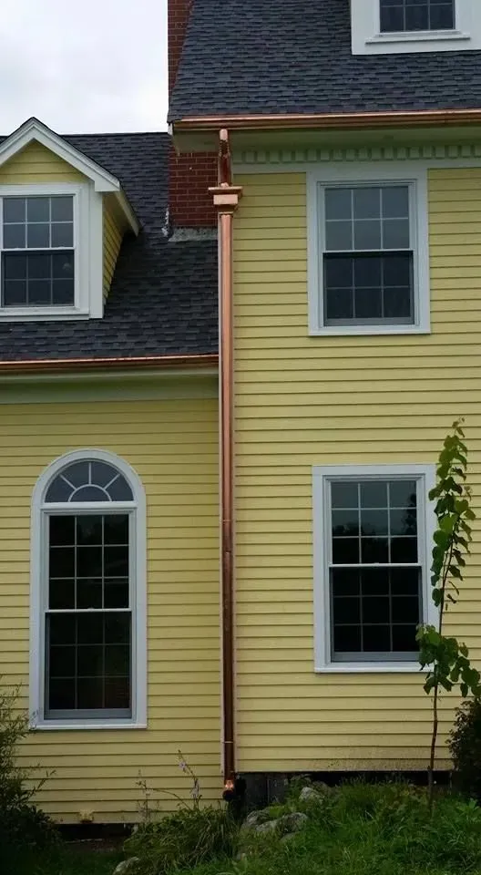 A yellow house with a copper gutter on the side