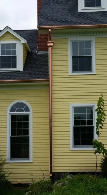 A yellow house with a copper gutter on the side