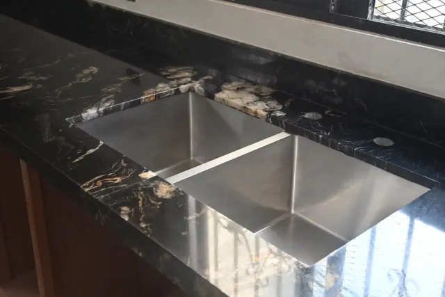 Double stainless steel sink in black granite countertop.