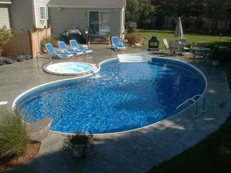 Backyard with a kidney-shaped swimming pool, a hot tub, lounge chairs, outdoor dining table with chairs, a grill, and a grassy yard with trees.