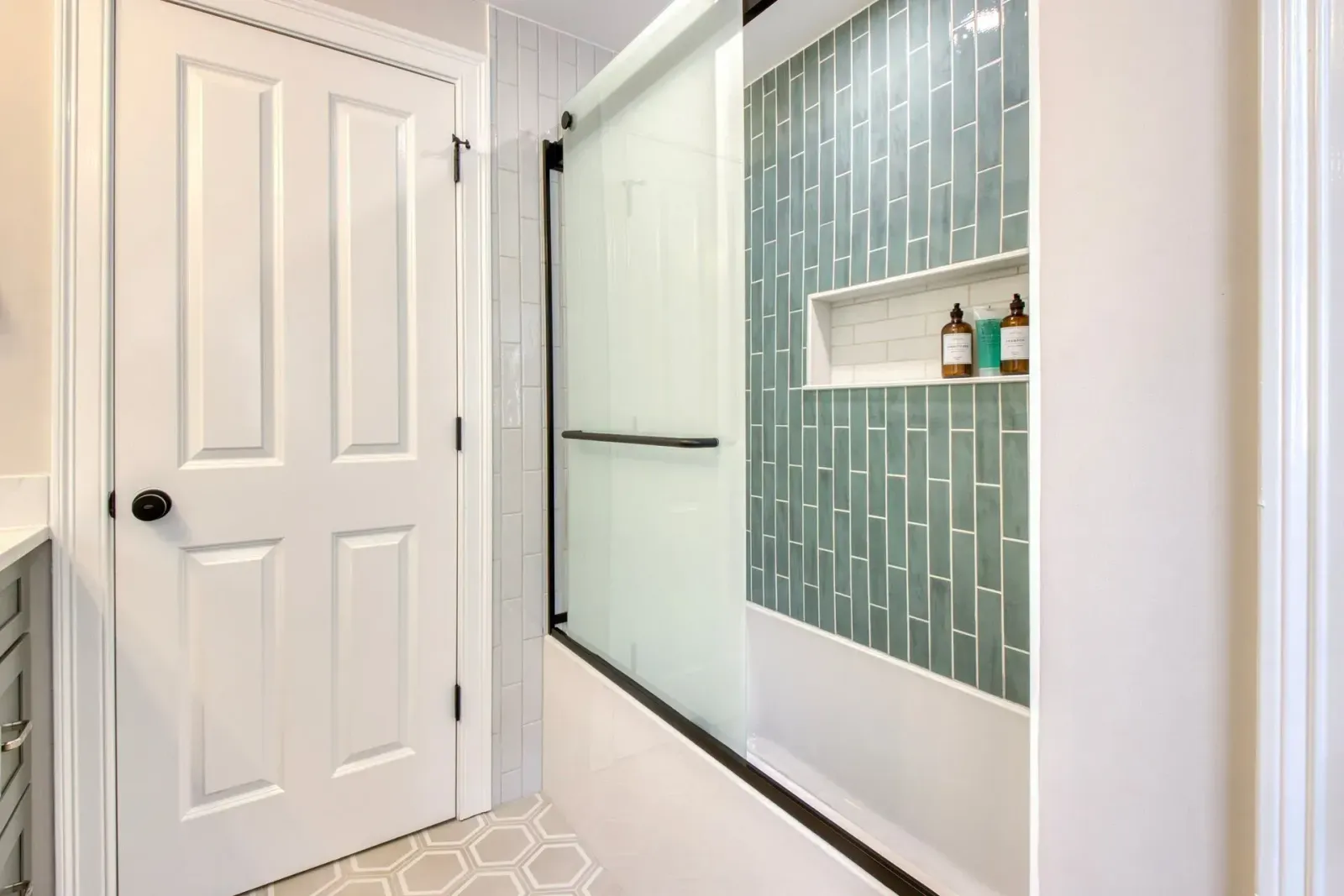 Bright bathroom with glass shower door, teal tile accent wall, and white paneled door.